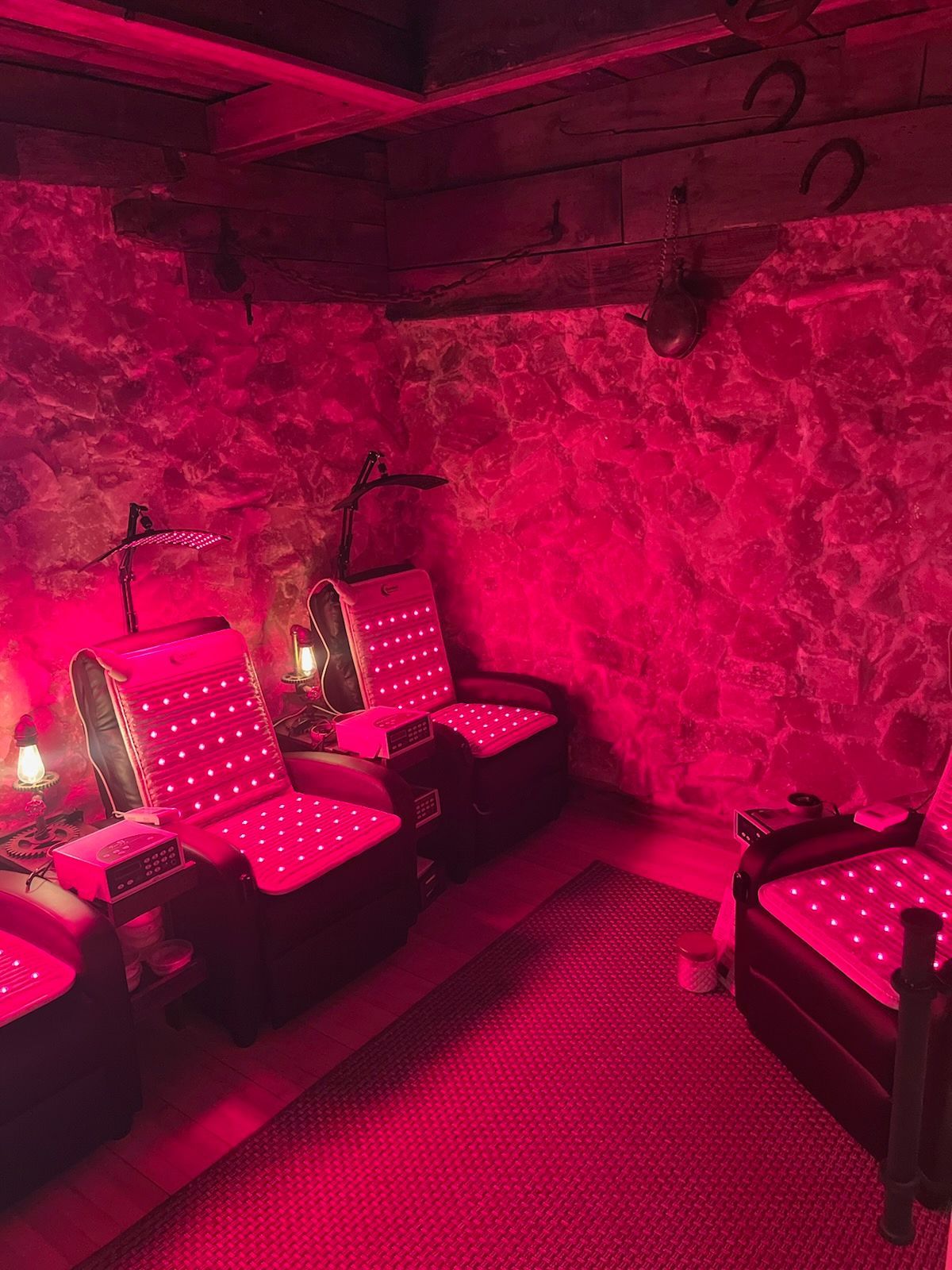 A room with stone walls and wooden beams features three dark chairs with glowing red light panels, bathed in red light.
