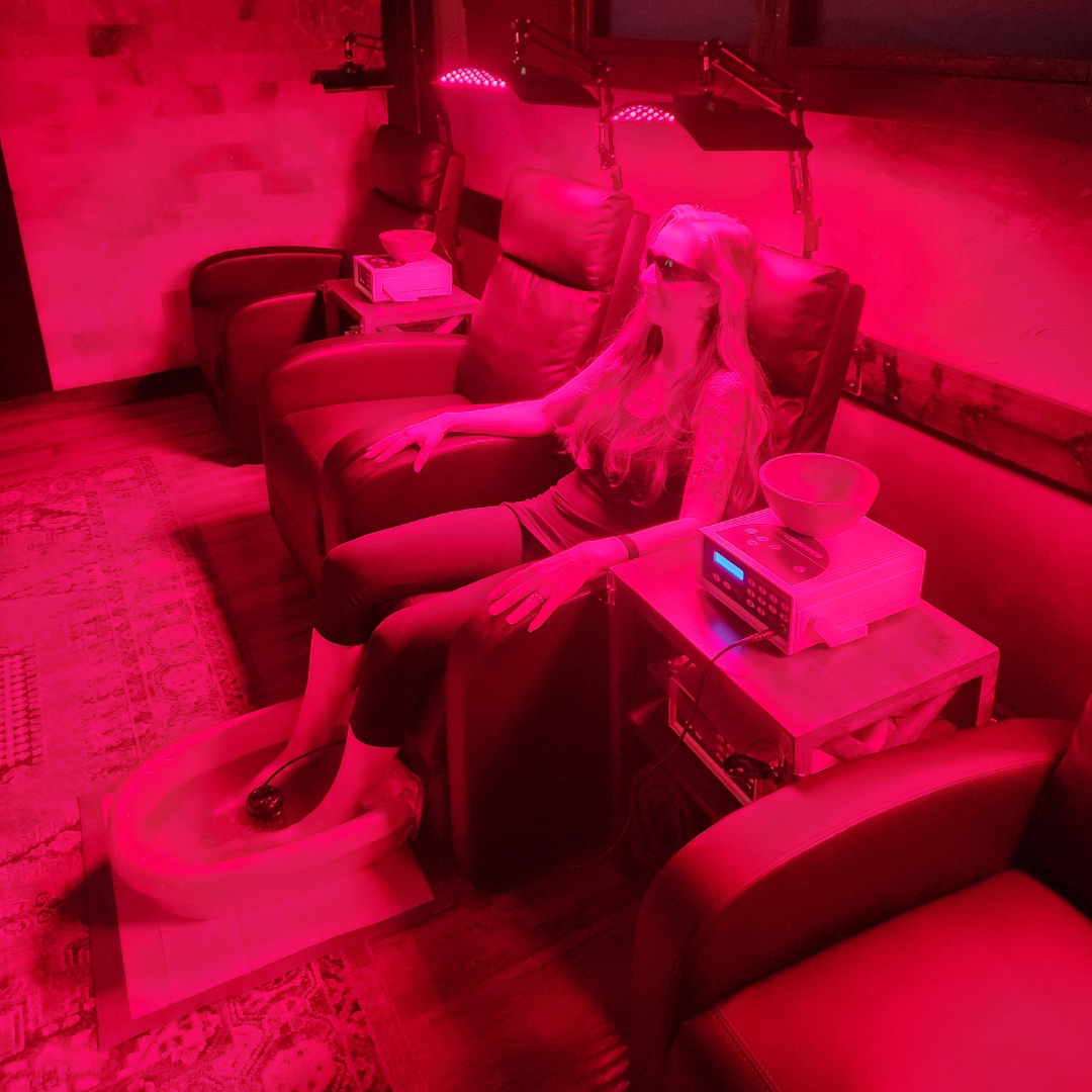 Woman relaxing on a red sofa, feet on a red mat, under red therapy lights.