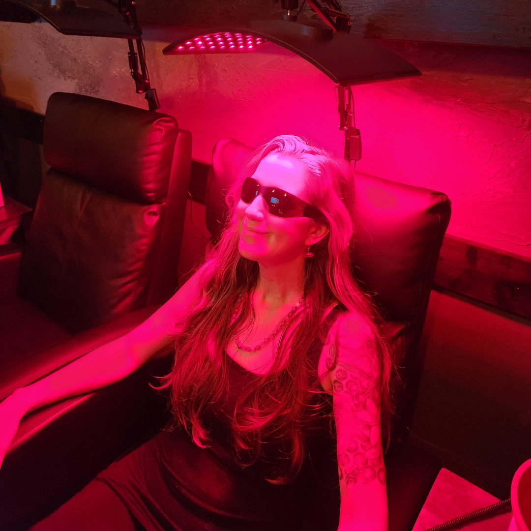 A woman wearing sunglasses is sitting in a chair under a red light.