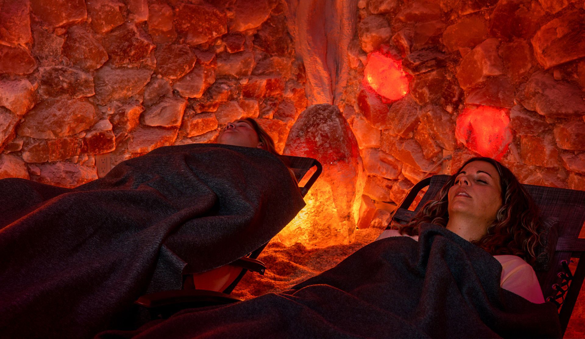 Two people relaxing in a salt cave, illuminated by red and orange lights.
