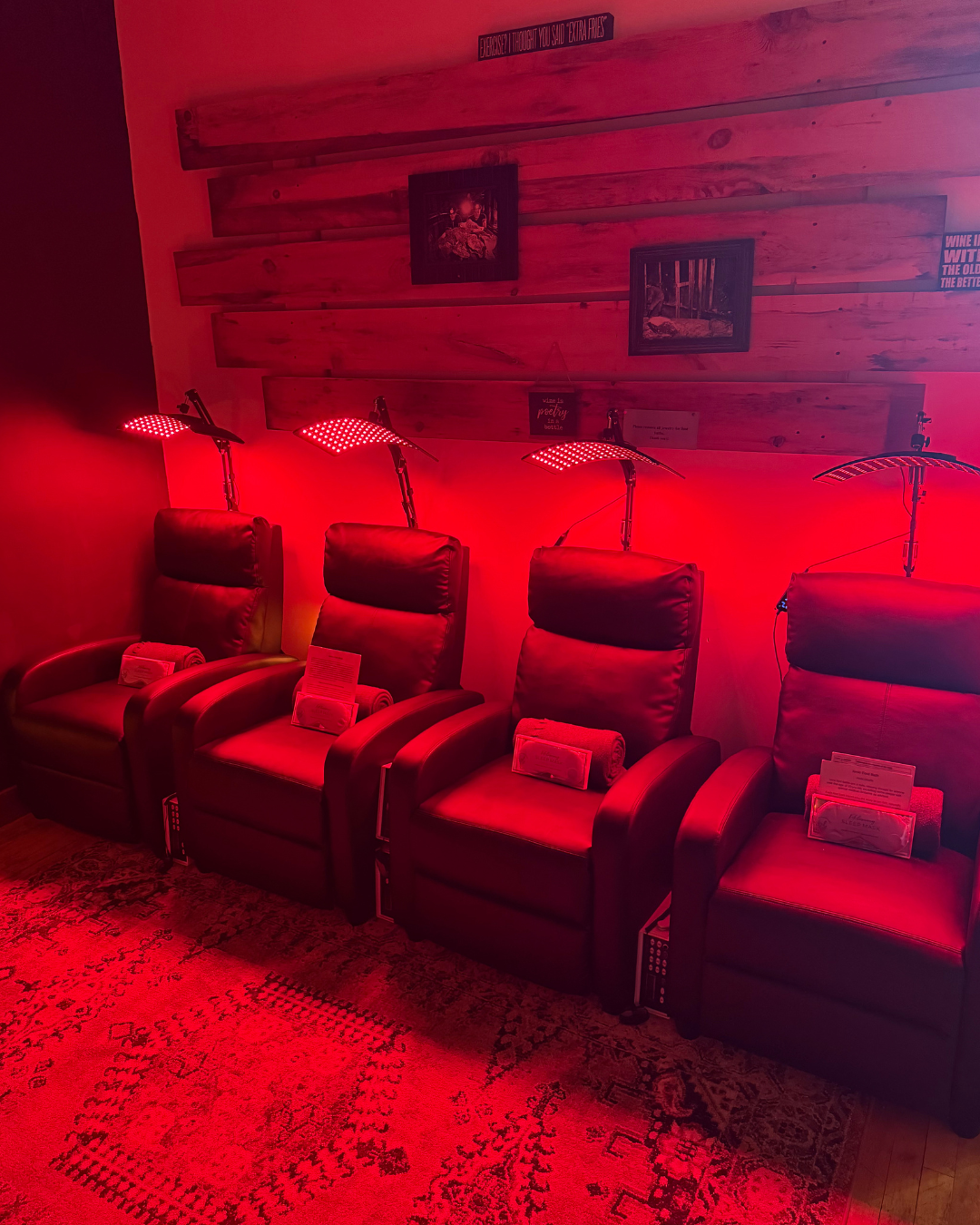 Four red recliners with red light therapy lamps in a room with wood paneling.