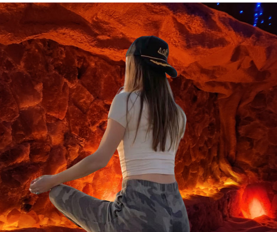 Woman in cap and camo pants sits in front of a red, glowing rock formation.