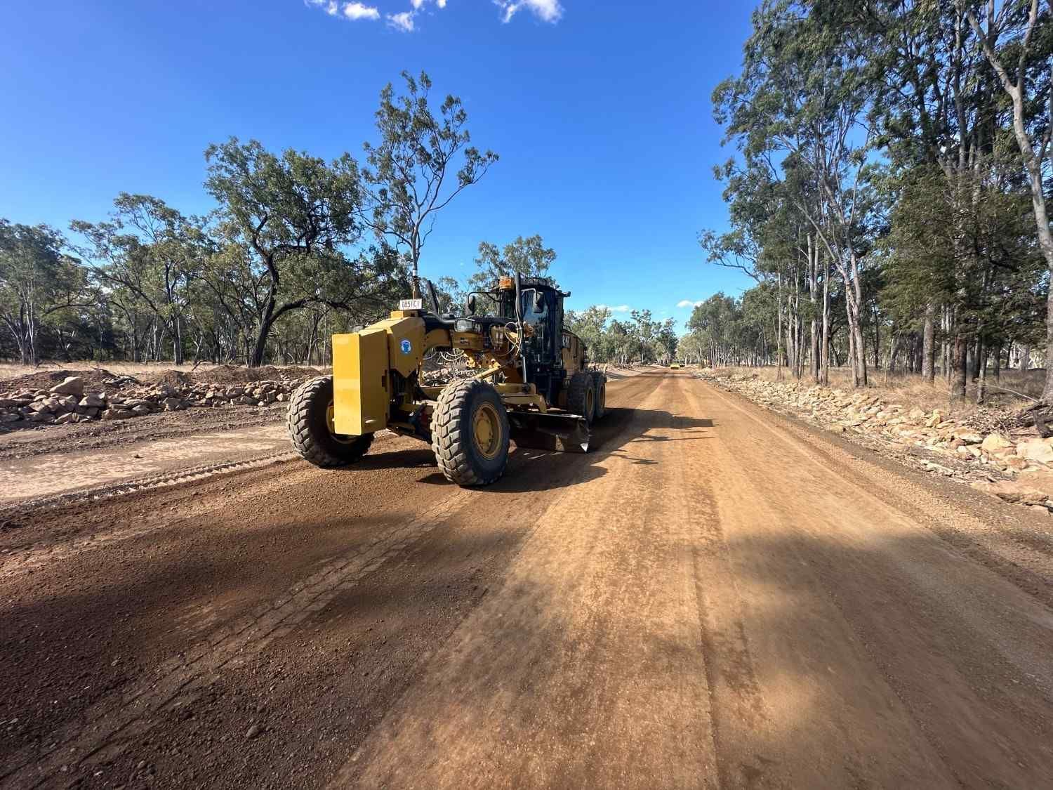 A Yellow Tractor Is Driving Down a Dirt Road  — L&V Civil Contracting in Park Ridge, QLD