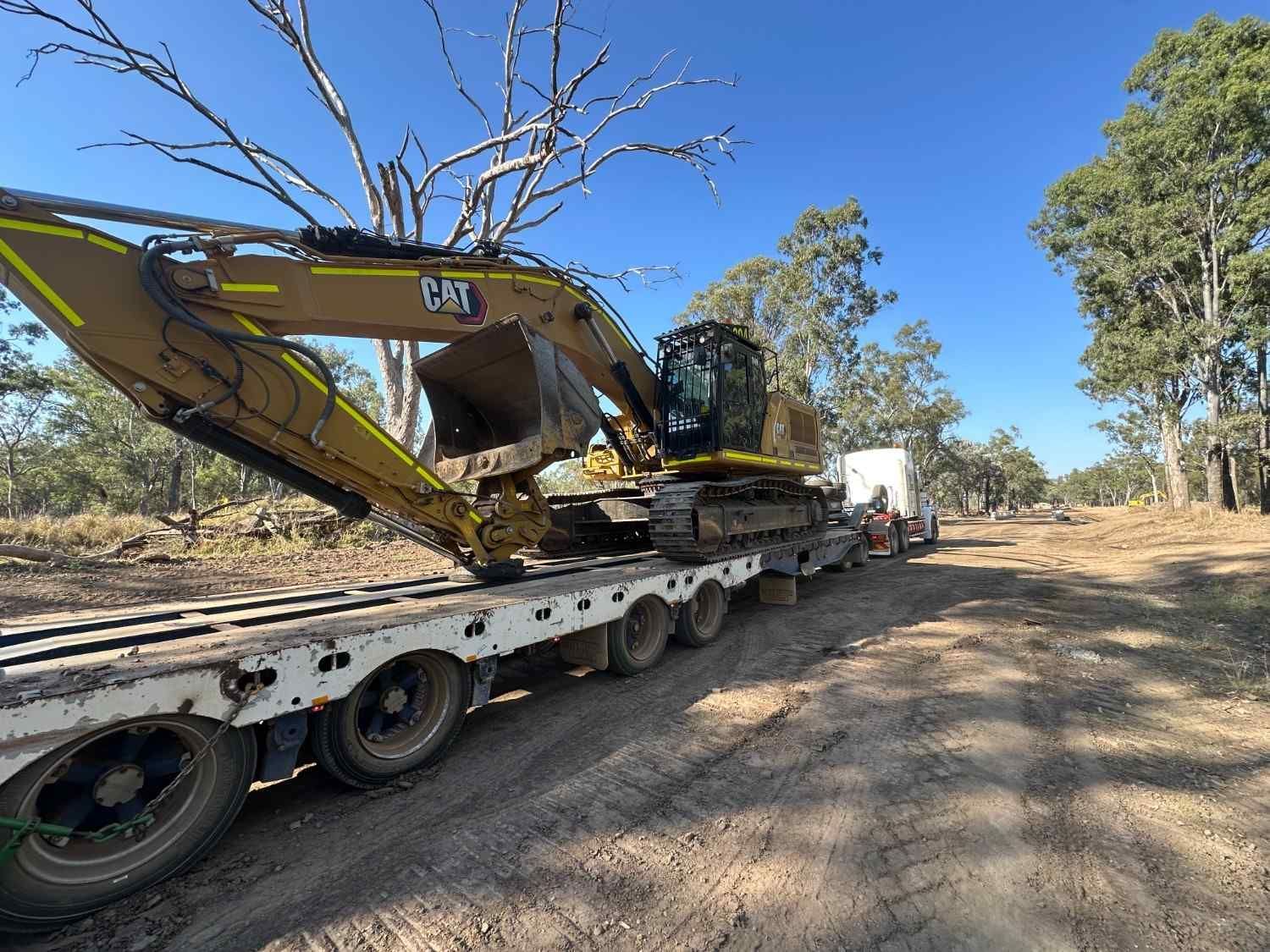 A Large Excavator Is Being Transported on A Trailer on A Dirt Road  — L&V Civil Contracting in Park Ridge, QLD