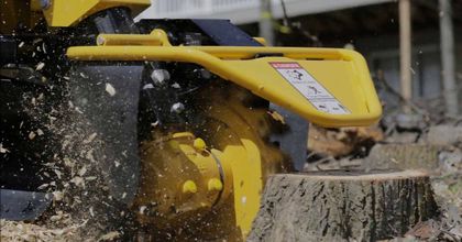 A yellow and black machine is cutting a tree stump.