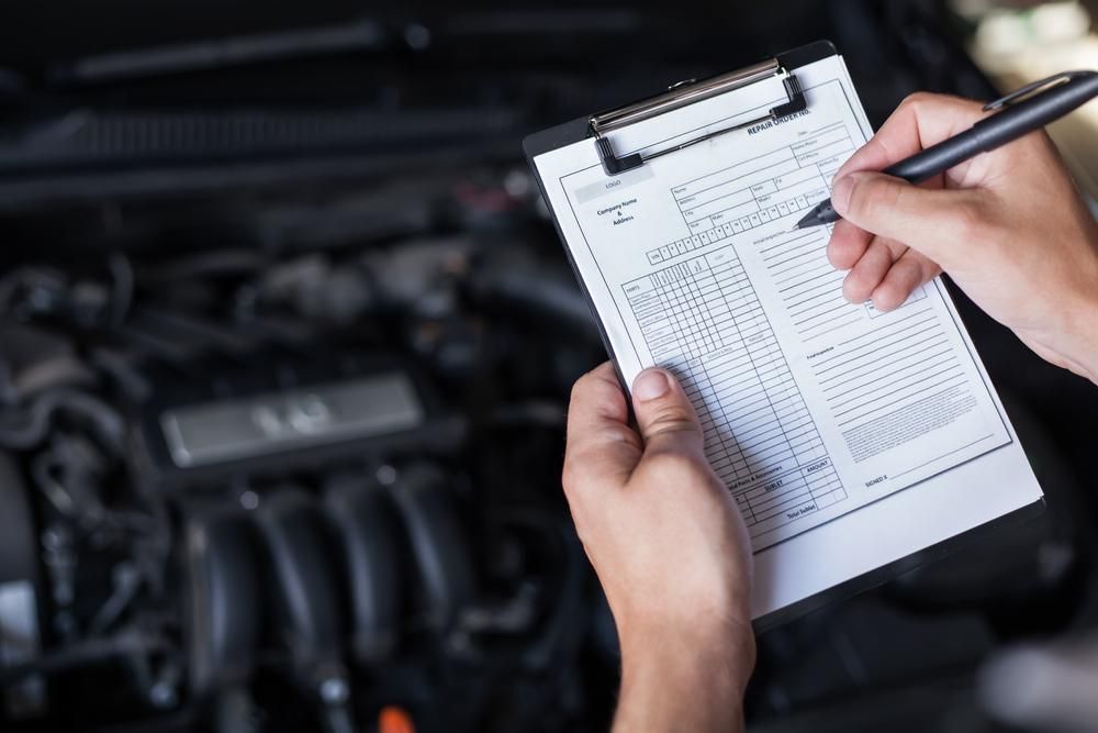 A Person is Writing on a Clipboard in Front of a Car Engine — Douglas Collision Management In Currajong, QLD