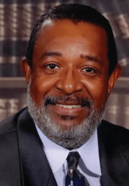 A man with a beard is wearing a suit and tie and smiling.