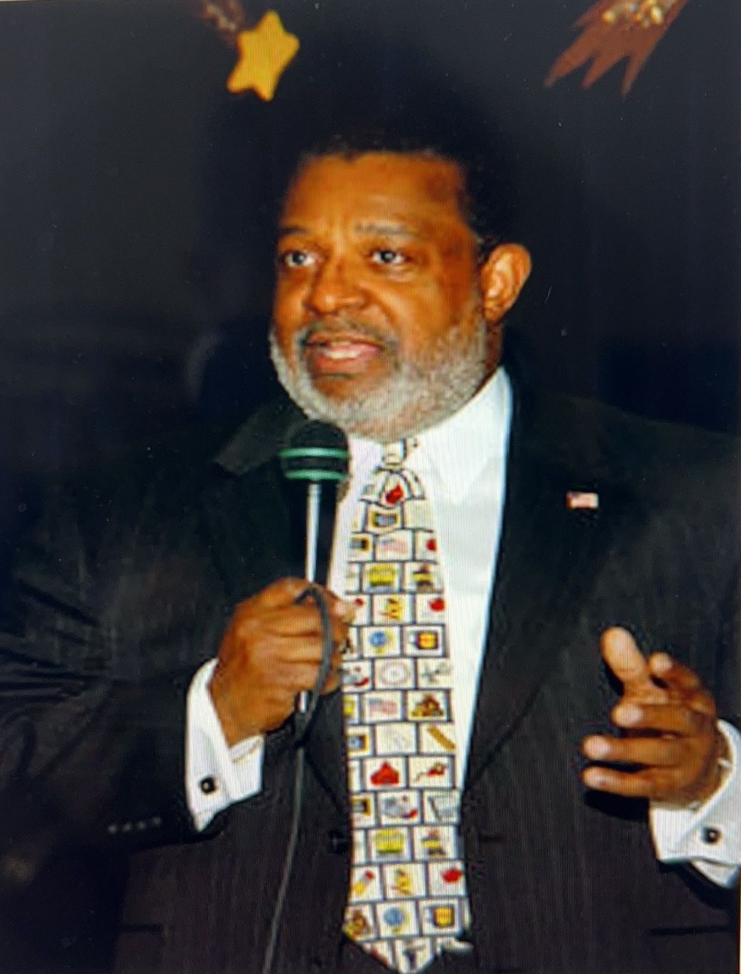 A man in a suit and tie is speaking into a microphone