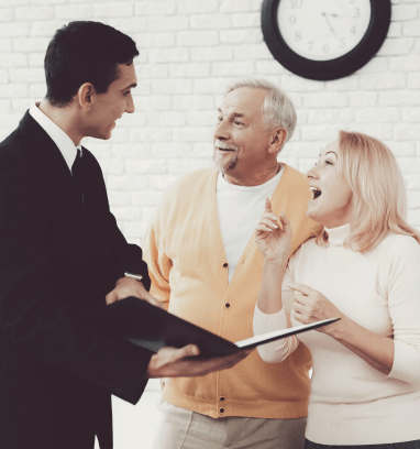 A woman is talking to a man and a woman while sitting at a table with a laptop.