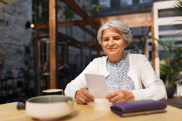 An elderly woman is sitting at a table reading a letter.