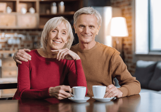 An elderly couple is sitting at a table with two cups of coffee.
