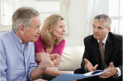 A man and a woman are sitting on a couch talking to a man in a suit.