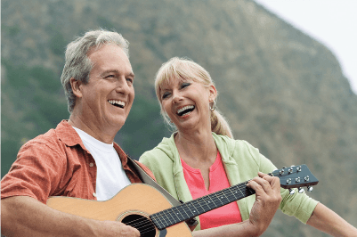 A man and a woman are laughing while a man plays a guitar.