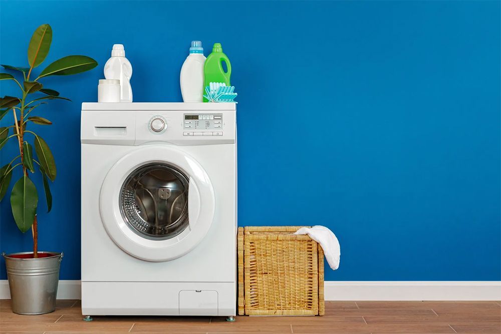 A white washing machine is sitting in a laundry room next to a wicker basket.