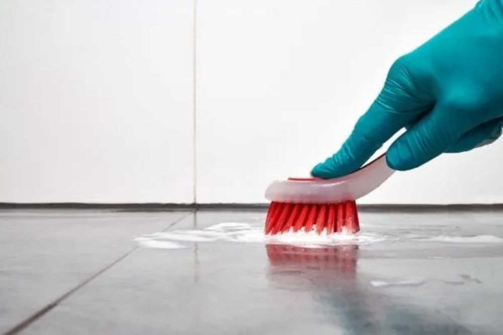 A person is cleaning a tile floor with a brush.