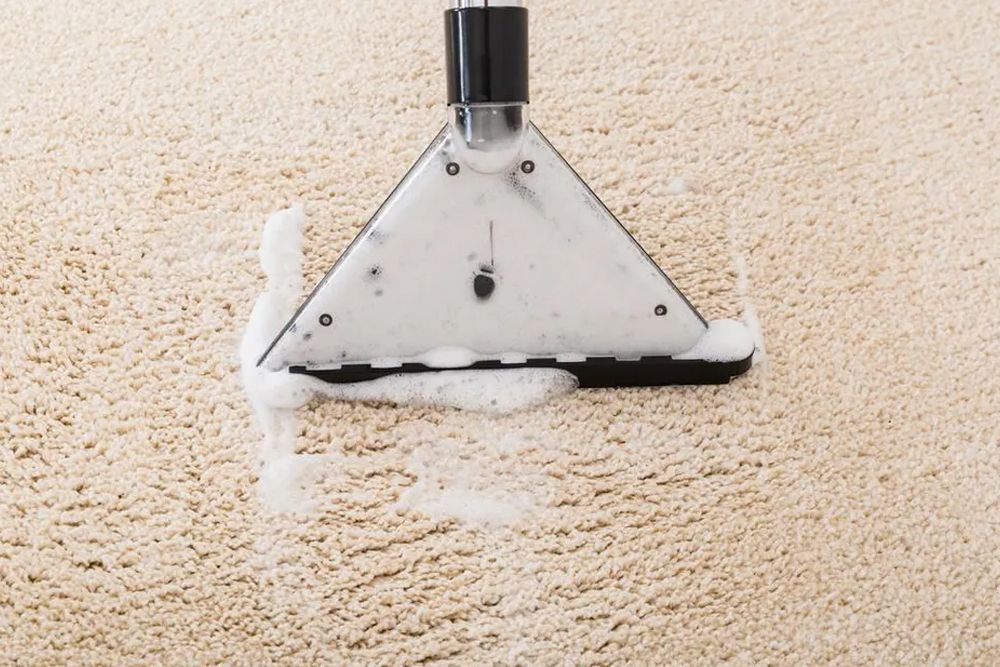 A vacuum cleaner is cleaning a carpet with foam coming out of it.