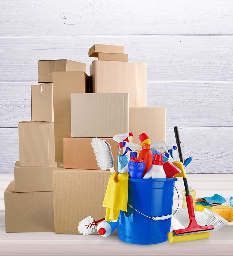 A blue bucket filled with cleaning supplies sits in front of a pile of cardboard boxes.