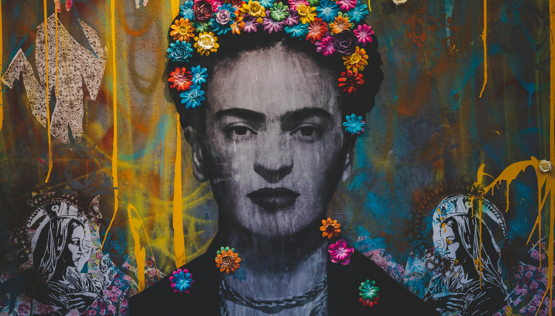 Retrato en blanco y negro de una mujer de expresión solemne, coronada por flores multicolores, sobre fondo urbano con graffiti.