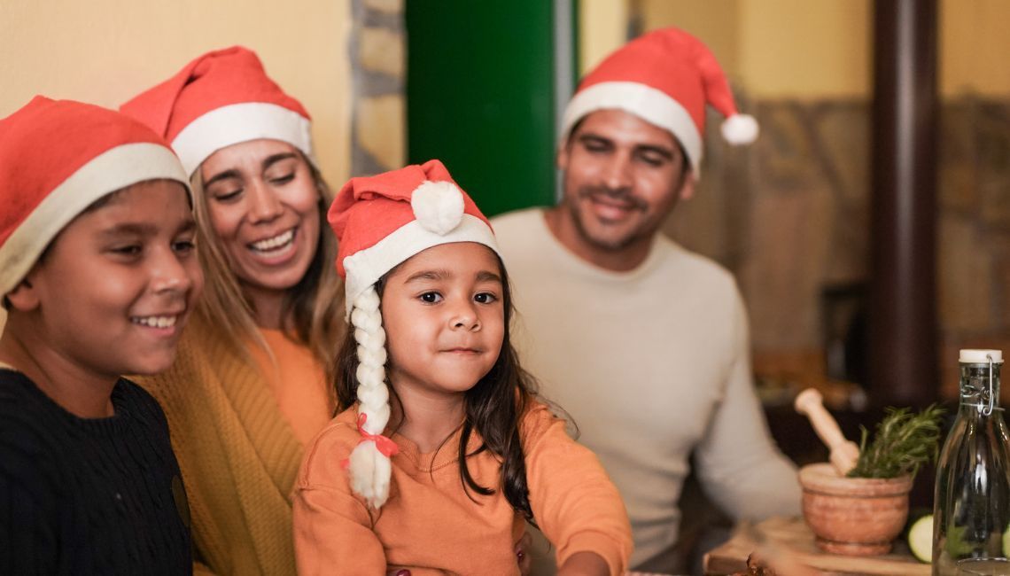 Familia celebrando la Nochebuena en casa, con niños y adultos usando gorros de Santa durante una cena navideña.