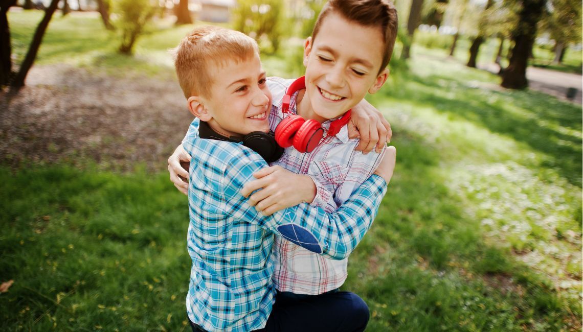 Niños hermanos abrazándose con alegría en un parque, reflejo del vínculo fraternal.
