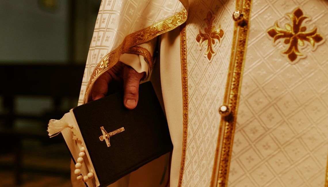 Figura religiosa católica con vestiduras litúrgicas ornamentadas, sosteniendo un libro sagrado.