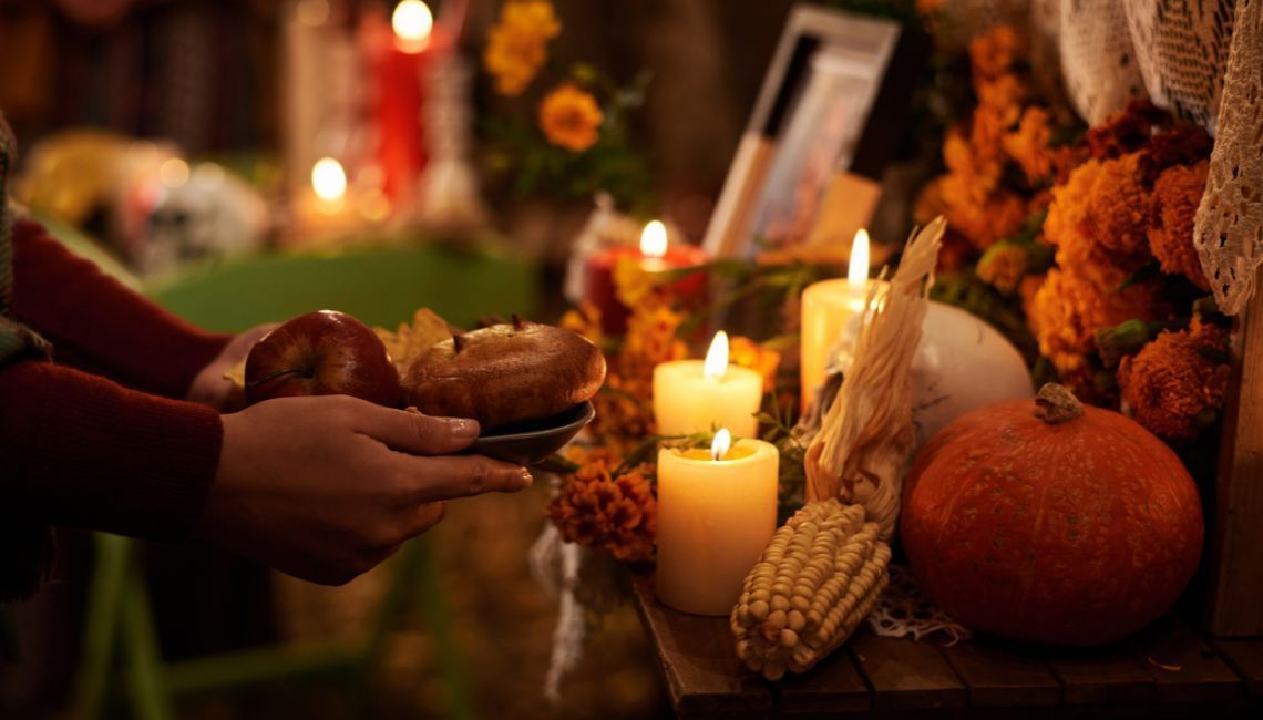 Detalle de ofrenda tradicional: velas, cempasúchil, calabaza y el gesto de entregar comida .