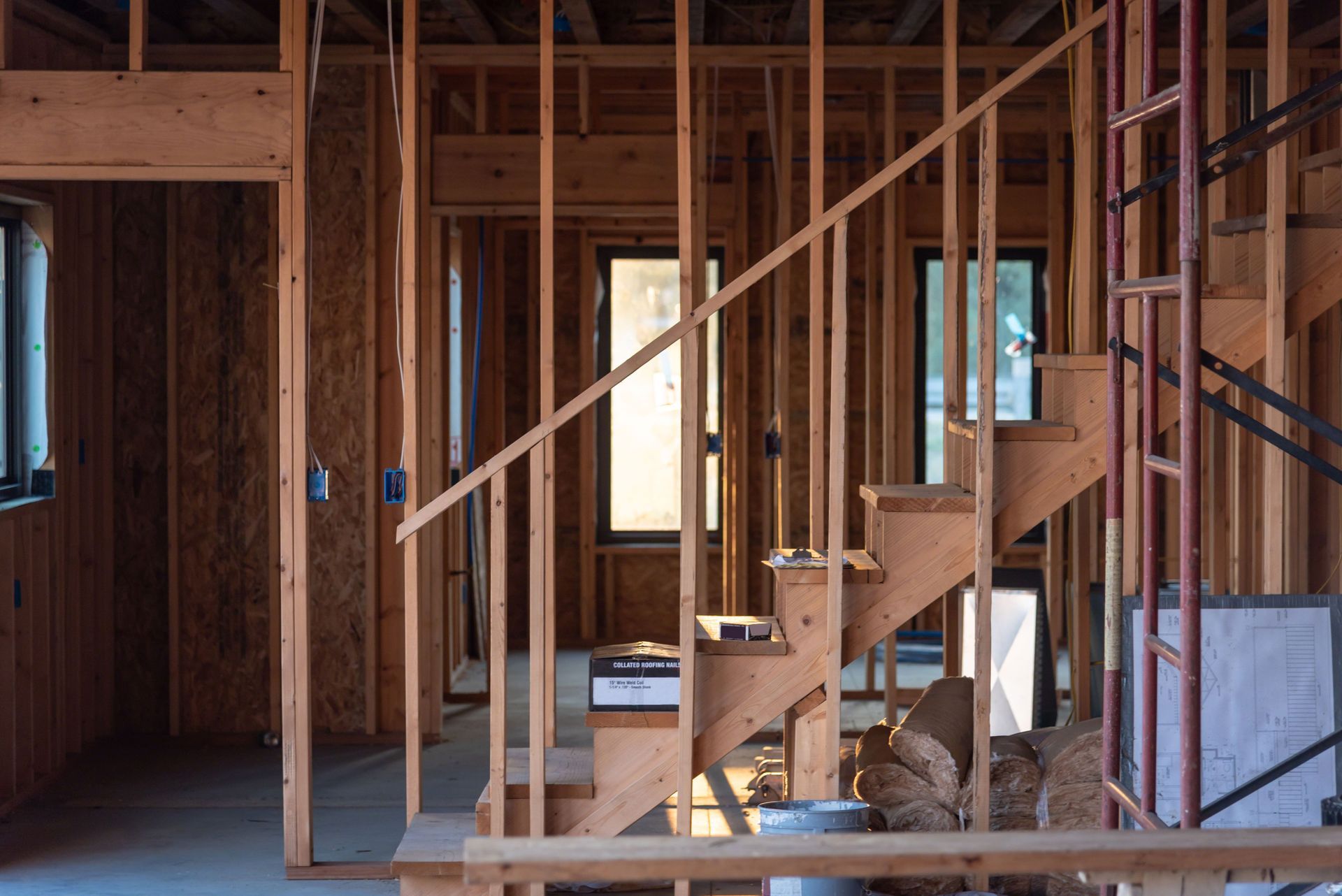 Interior of a house under construction; wooden studs frame a staircase and windows.