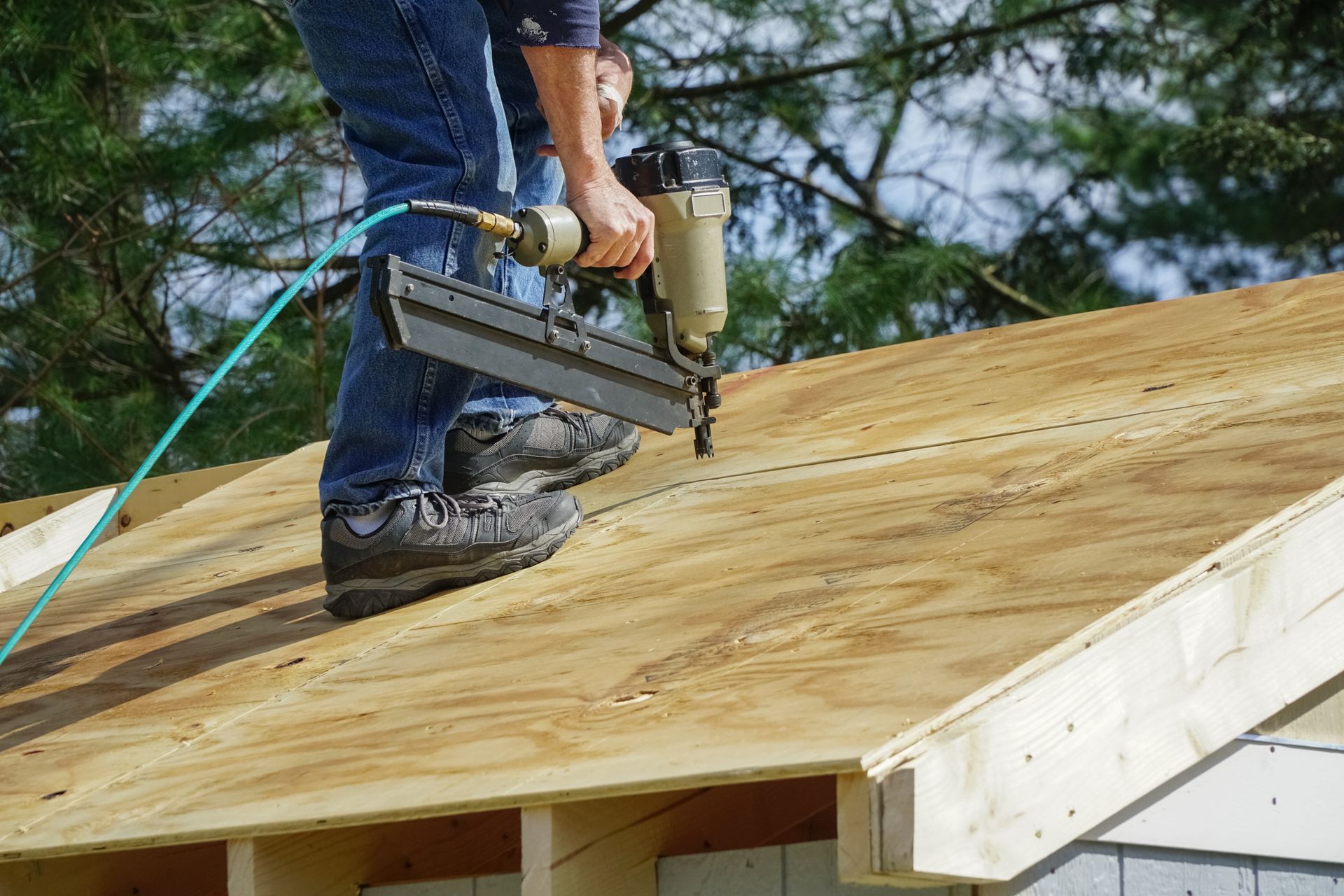 Person using a nail gun to fasten plywood to a wooden roof frame.