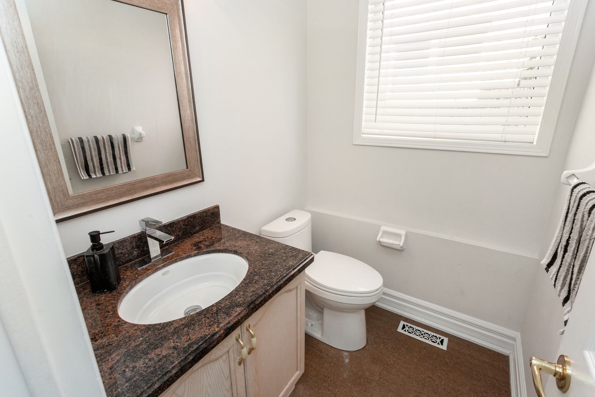 Bathroom with a brown granite countertop, a white toilet, and a window with blinds.