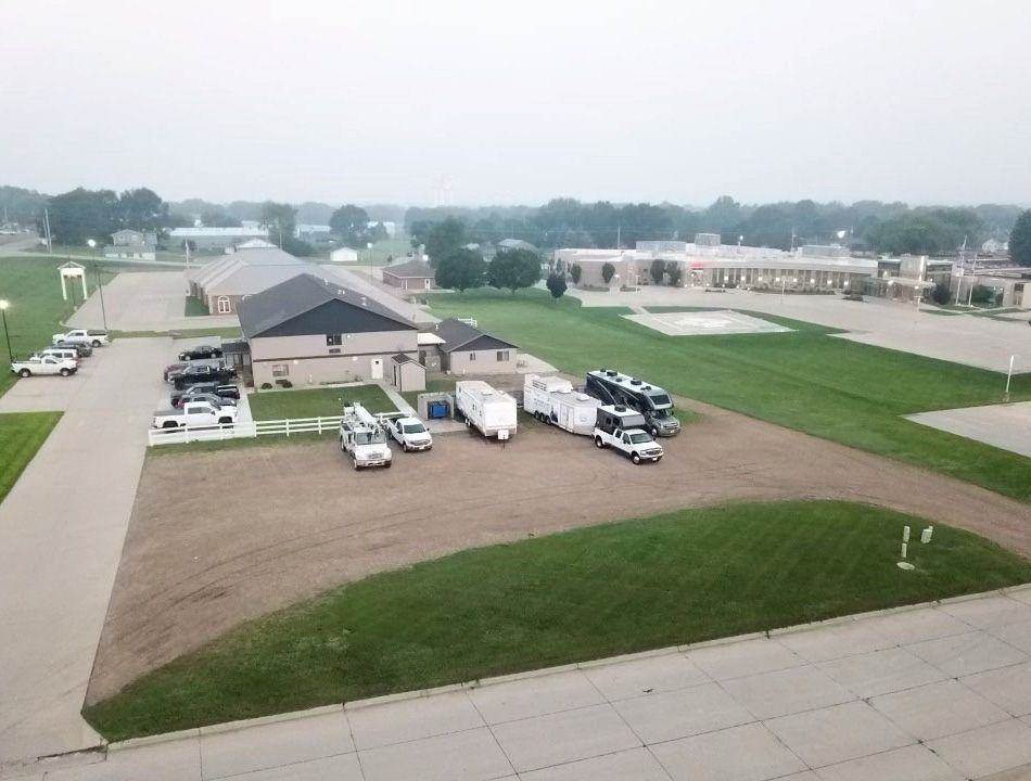 Vehicles parked on dirt and grass near buildings in a town, overcast sky.