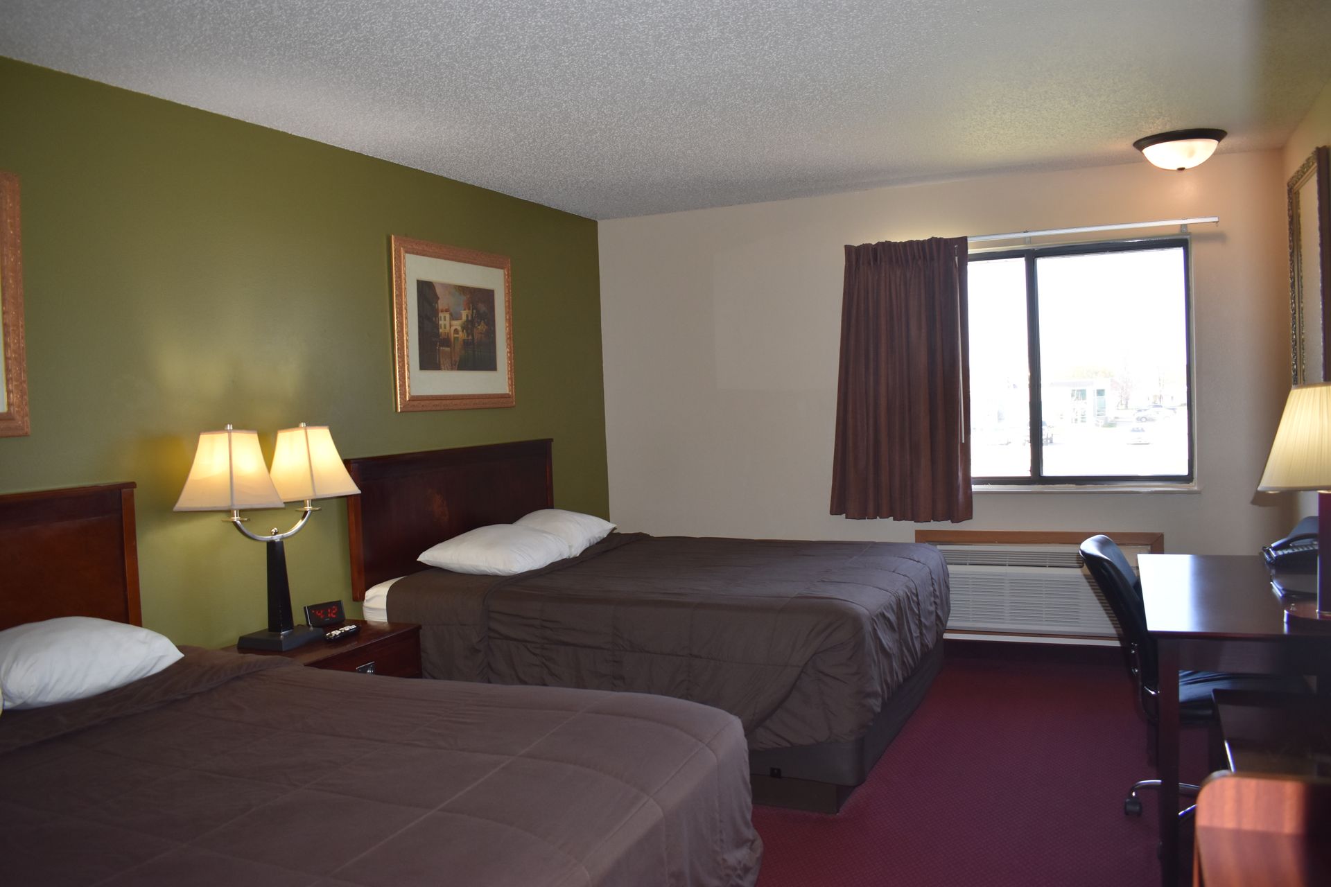 A hotel room with two beds , a desk and a window.