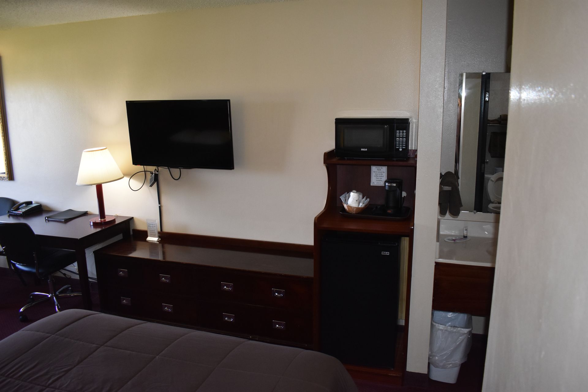 A hotel room with a bed , desk , television , microwave and refrigerator.