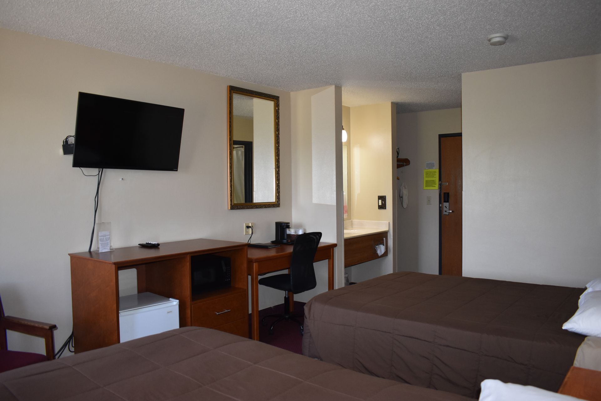 A hotel room with two beds , a desk , a flat screen tv and a mirror.