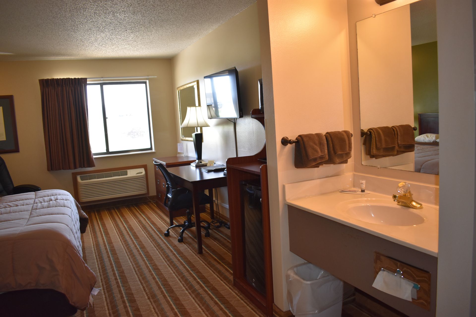 A hotel room with a bed , desk , sink and mirror.