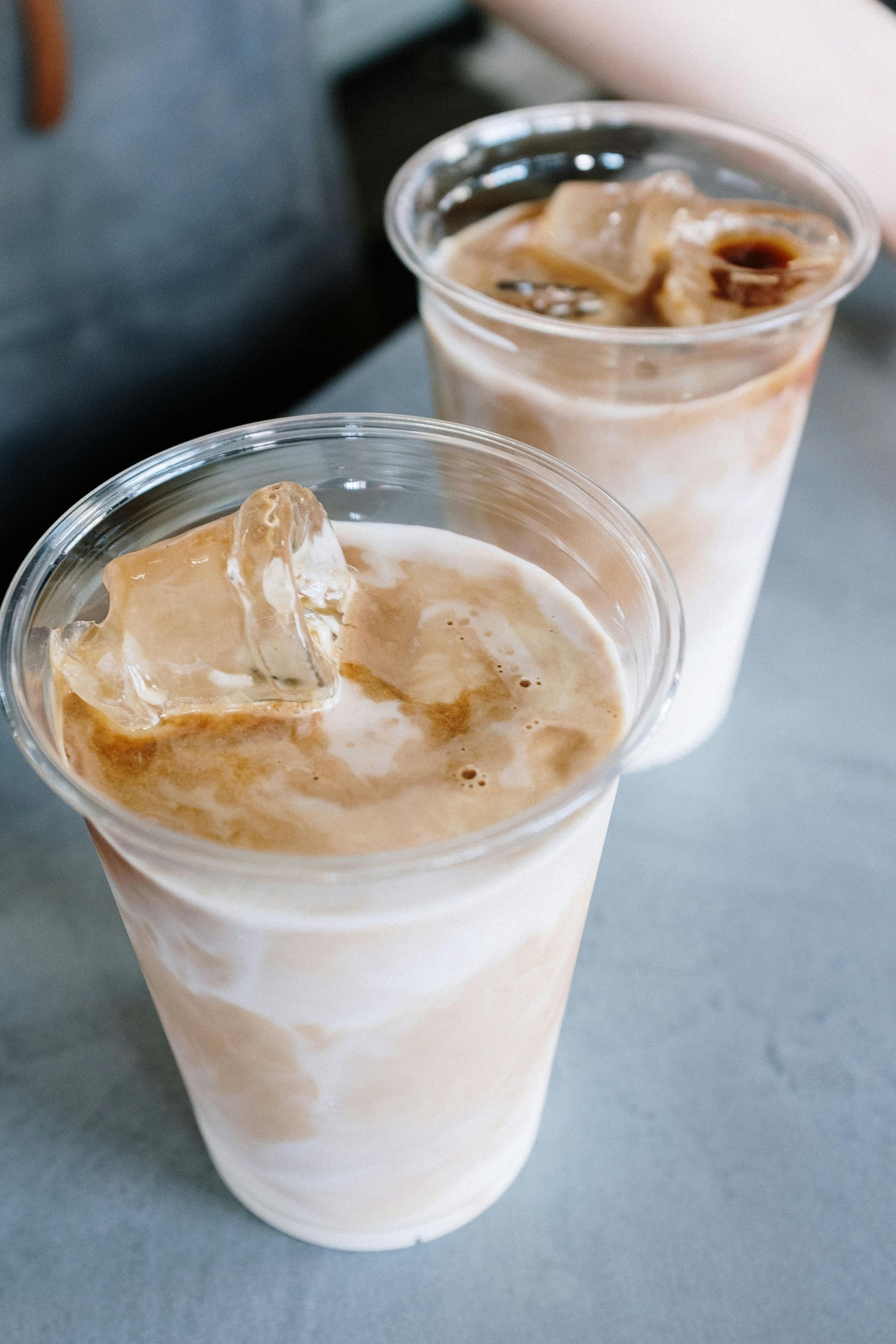 Two cups of iced coffee with ice cubes on a table.