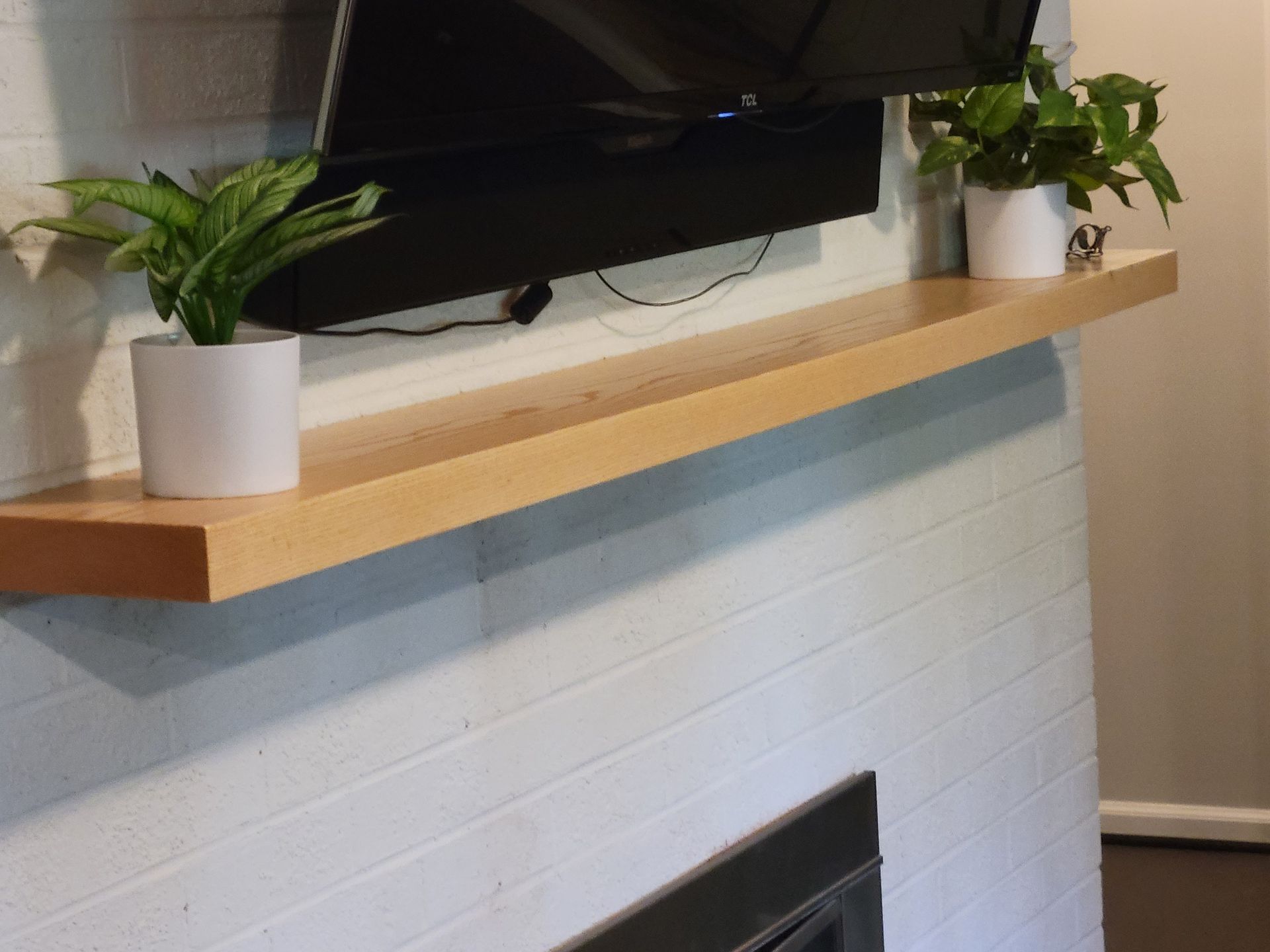 Two potted plants sit on a wooden shelf above a fireplace