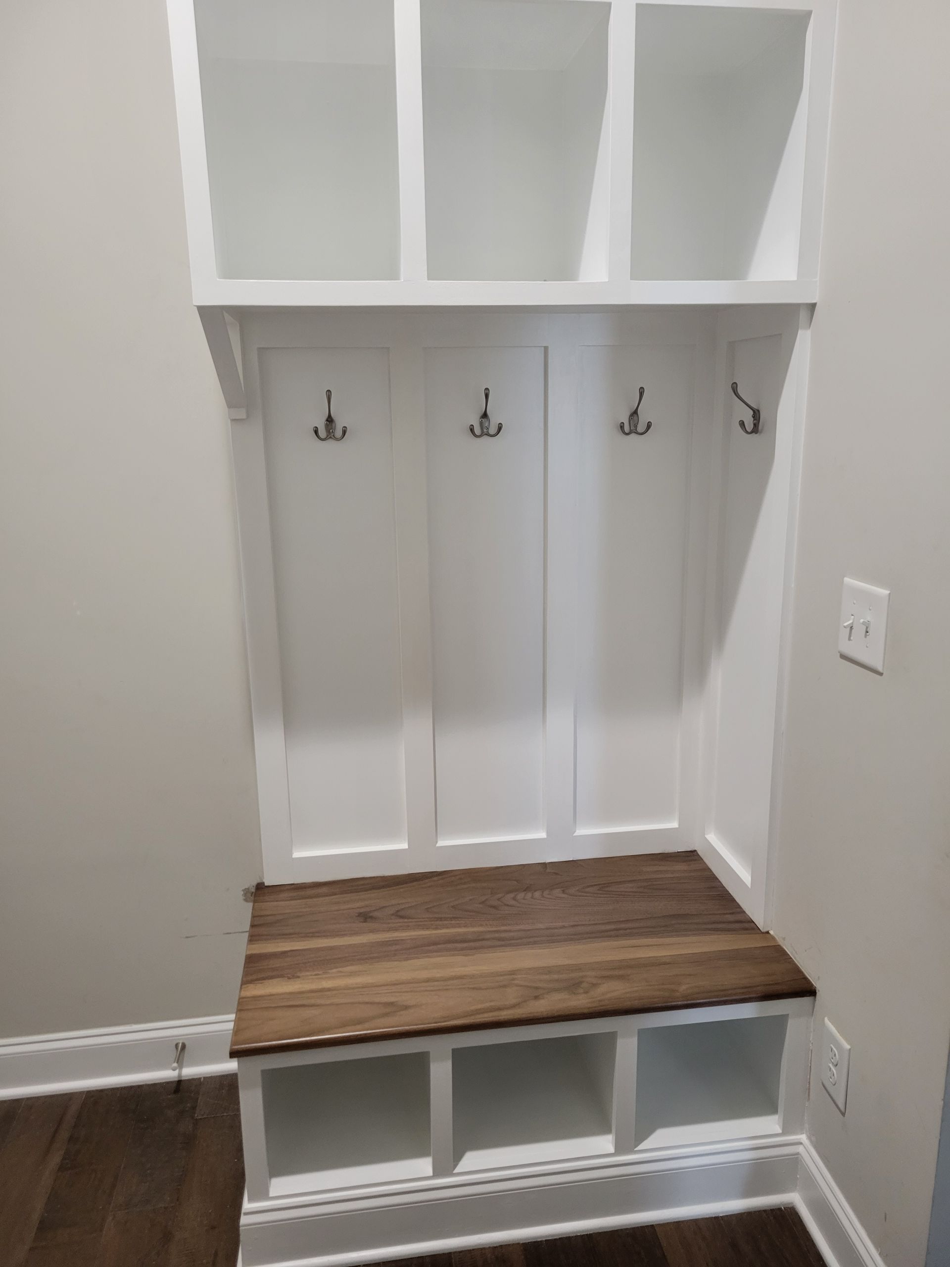 A white coat rack with hooks and a wooden bench in a hallway.