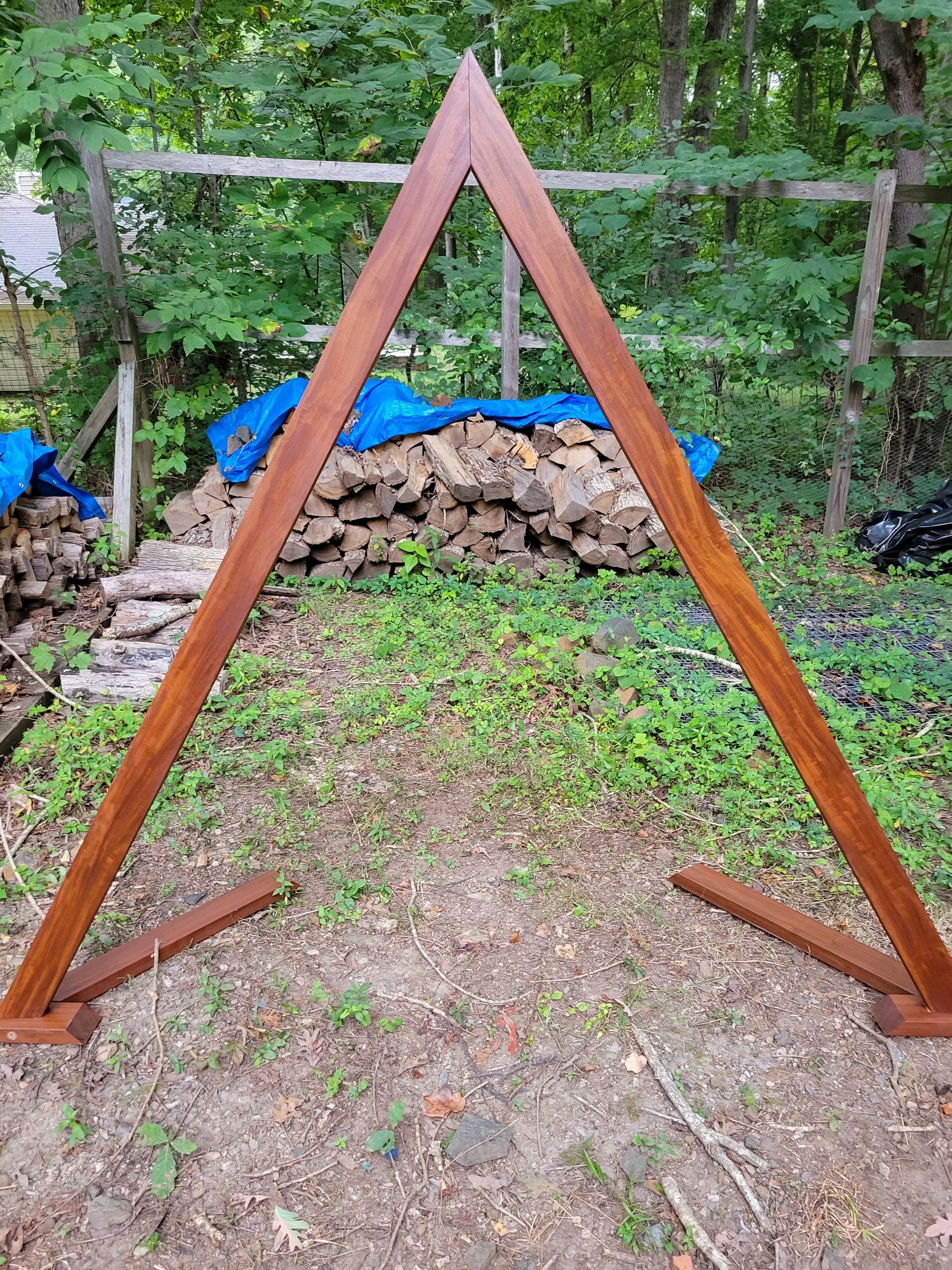 A wooden arch is sitting in the dirt in front of a pile of logs.