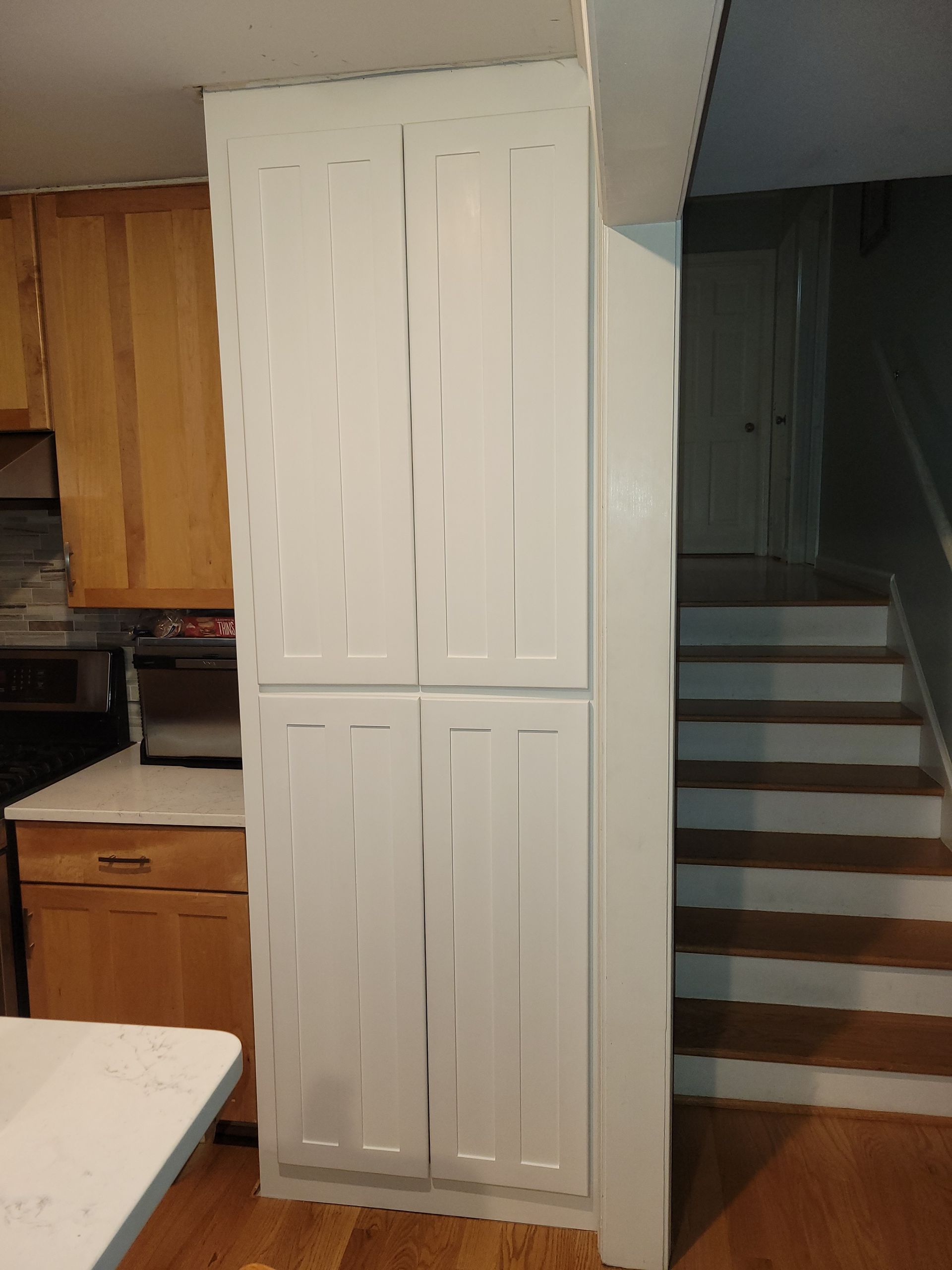 A kitchen with white cabinets and wooden cabinets and stairs