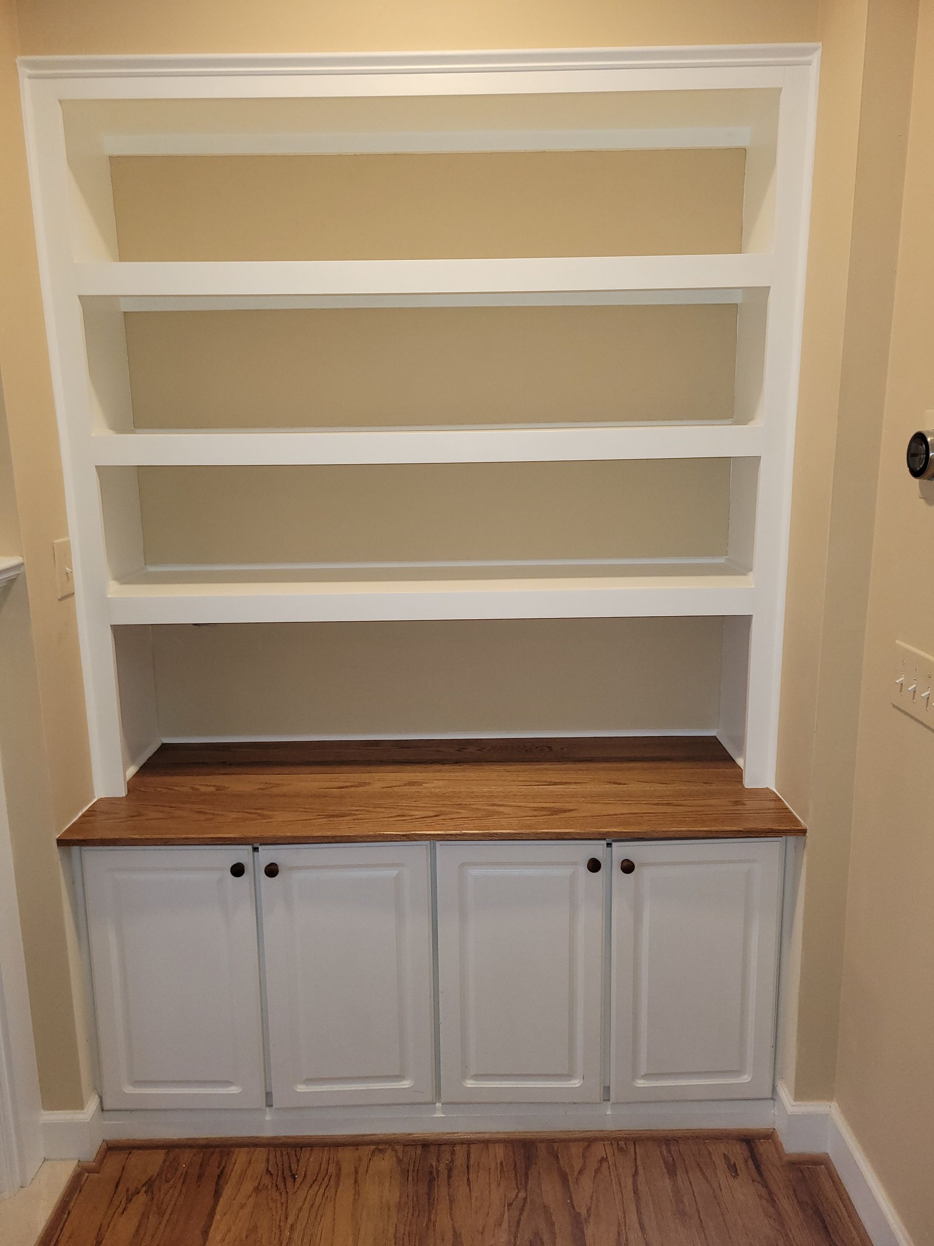 A bookshelf with wooden shelves and cabinets in a room with hardwood floors.