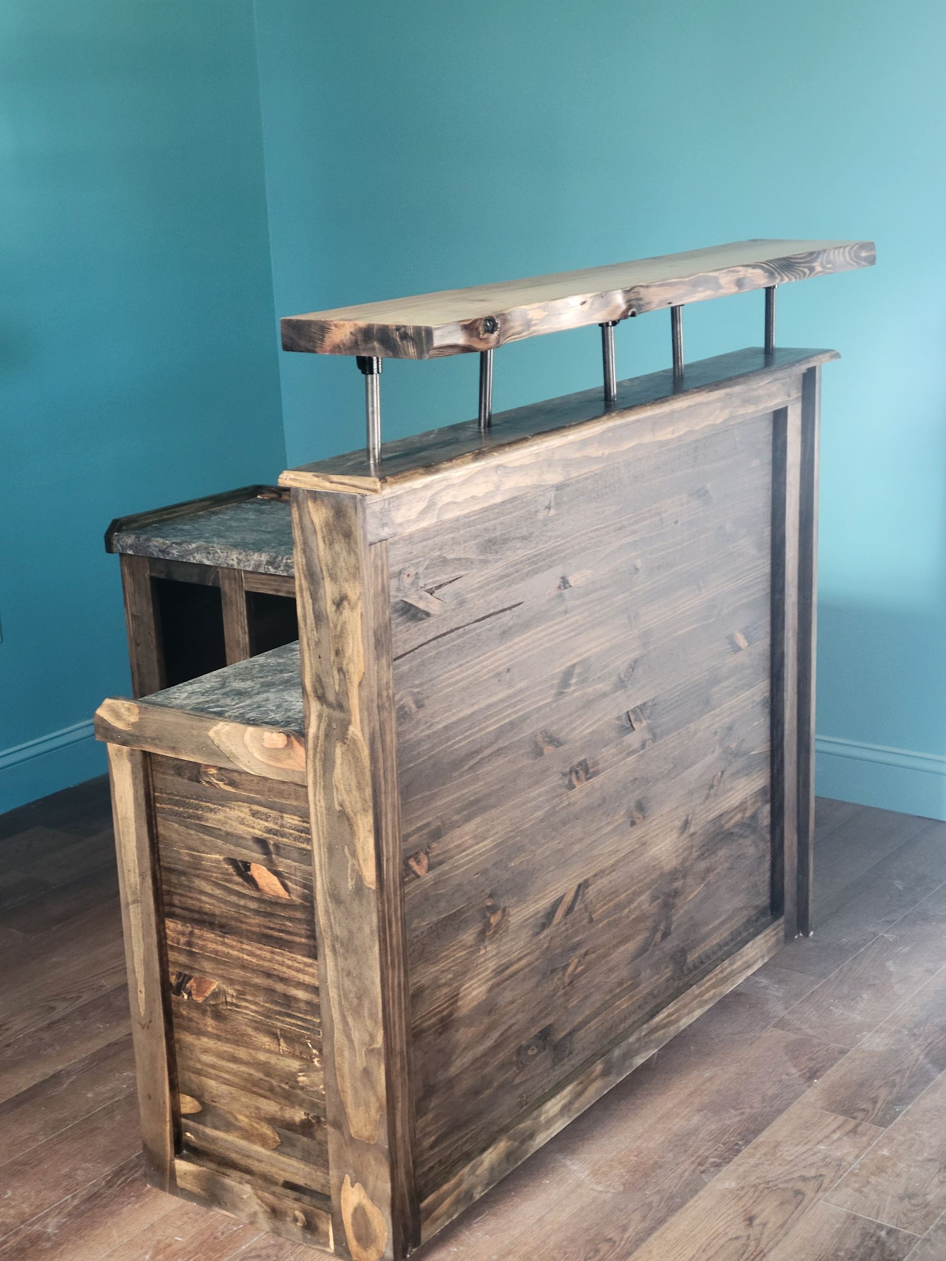 A wooden bar with a marble top is sitting on a wooden floor in a room.