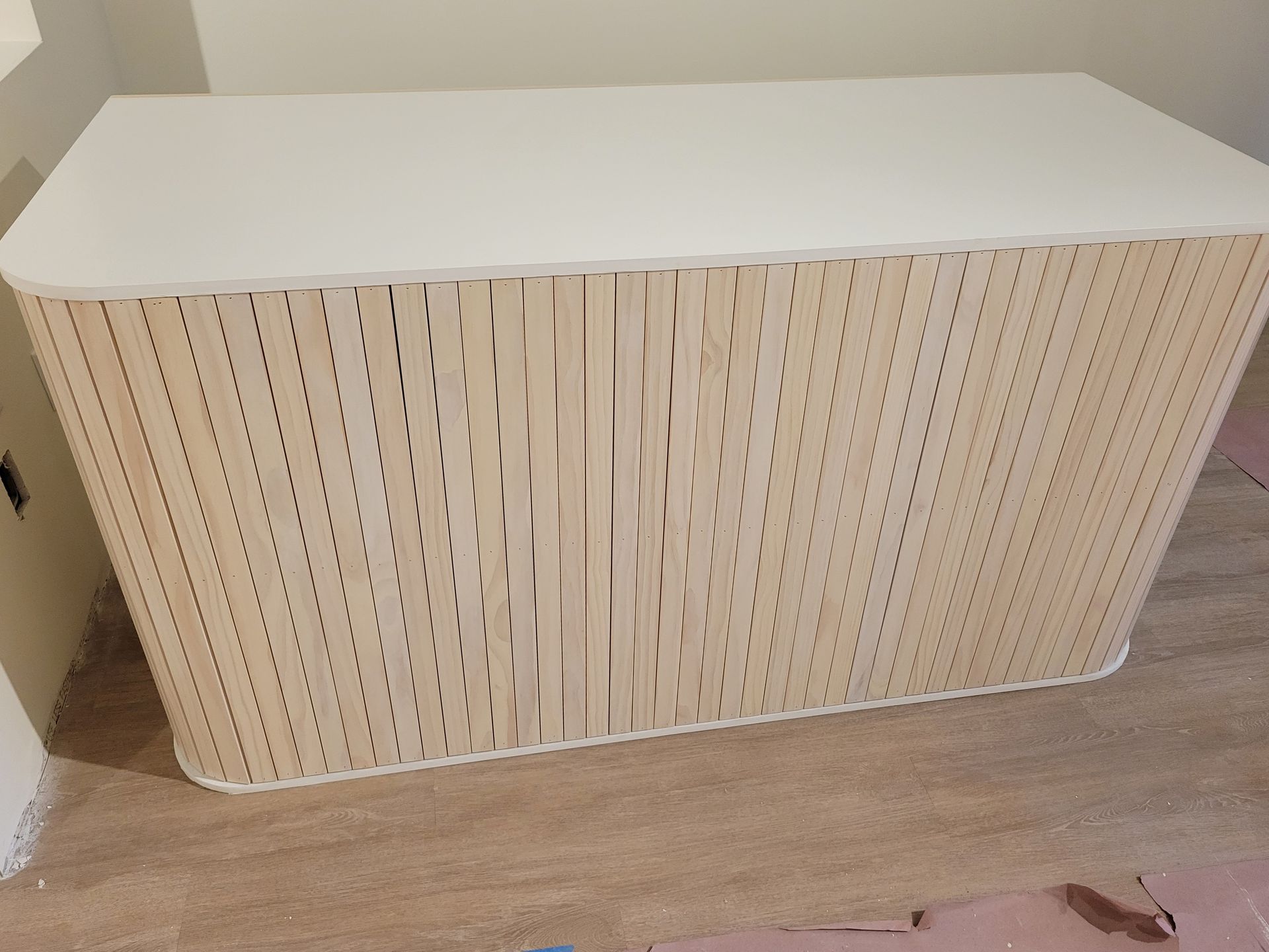 A wooden cabinet with a white top is sitting on a wooden floor.