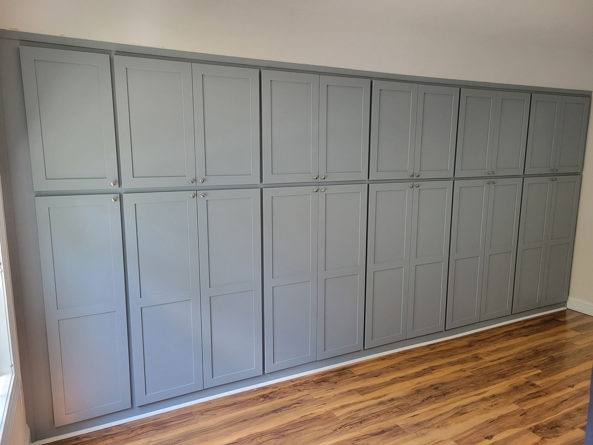 A large wall of gray cabinets with wooden floors in a room.