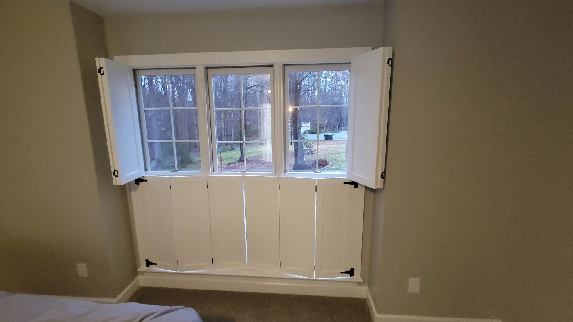 A bedroom with a large window and white shutters.