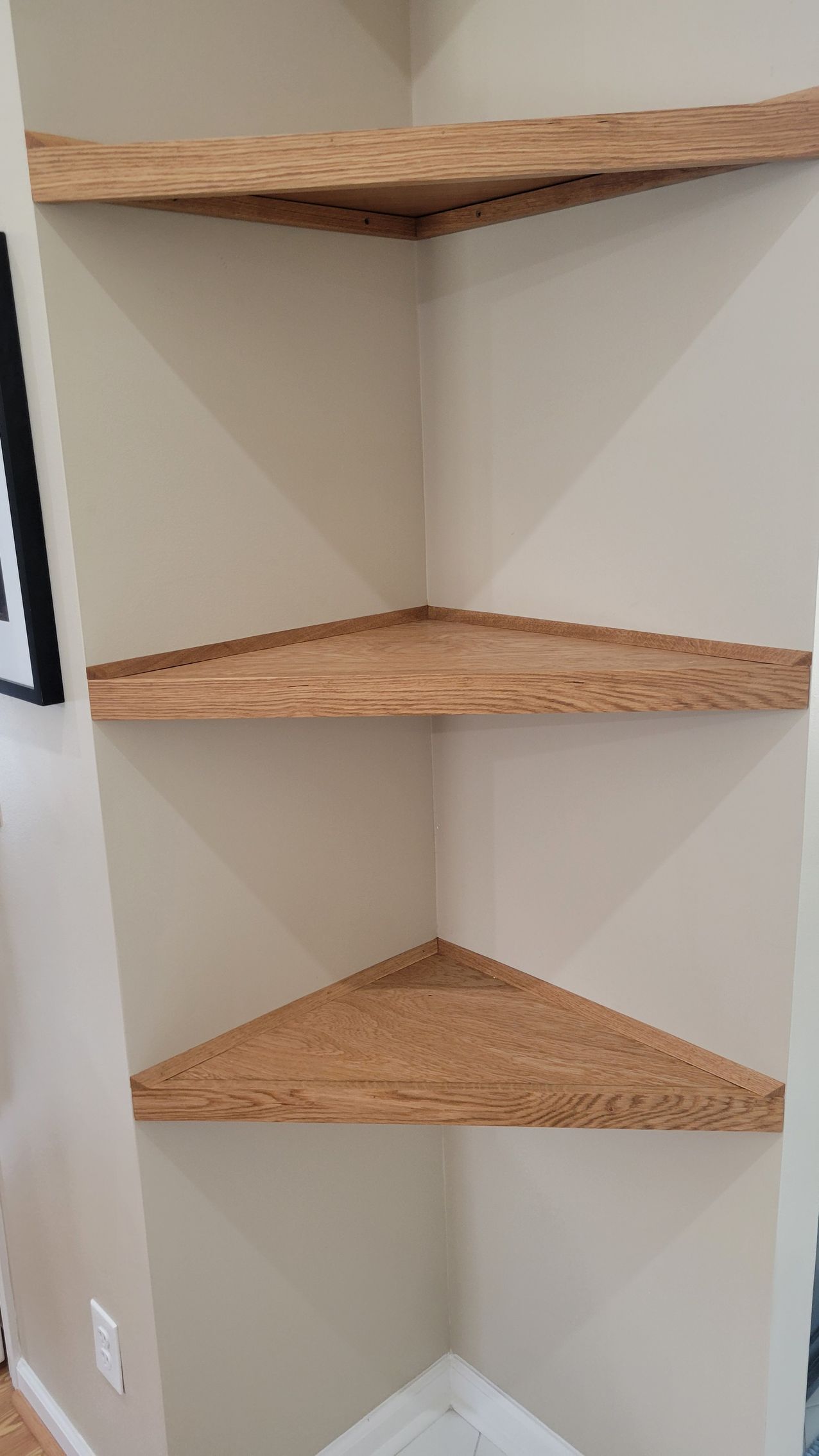 A corner shelf with three wooden shelves in a room.