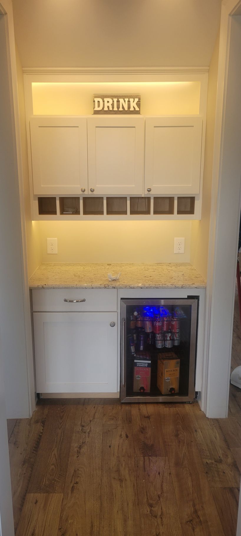 A kitchen with white cabinets , a refrigerator and a sign that says `` drink ''.