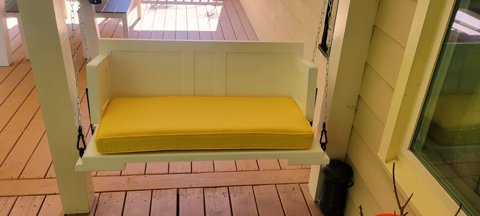 A porch swing with a yellow cushion is hanging from the side of a house.