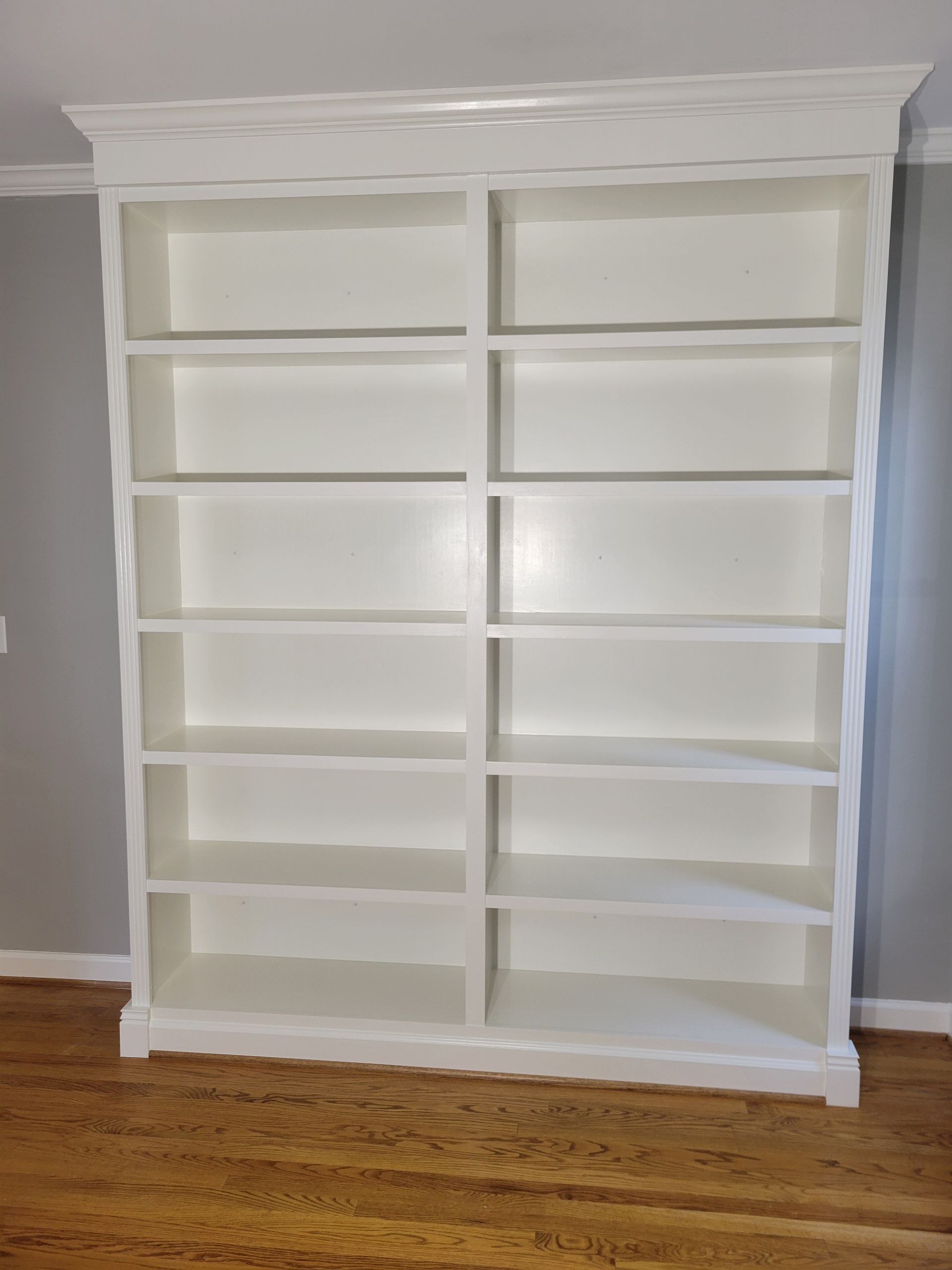 A large white bookshelf is sitting on a wooden floor in a room.