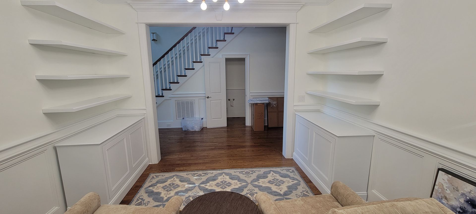 A living room with white shelves and a staircase in the background.