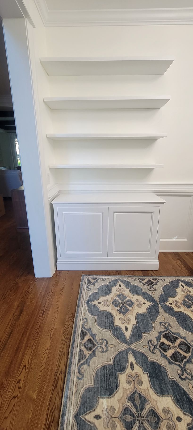 A living room with hardwood floors , white shelves , and a rug.